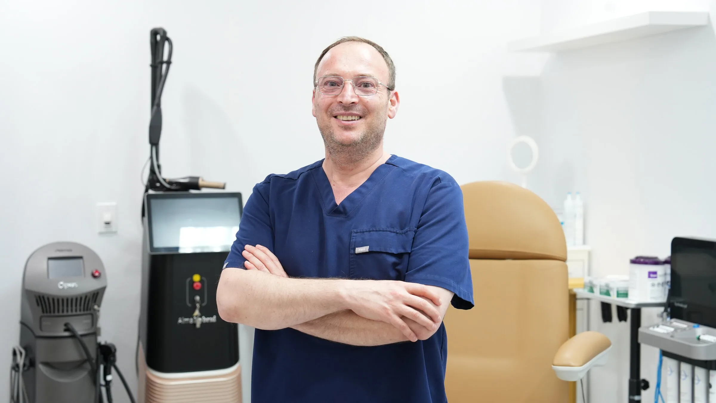 Dr. Maher Danhash standing with his arms folded in a treatment room at the Upland office, wearing navy scrubs