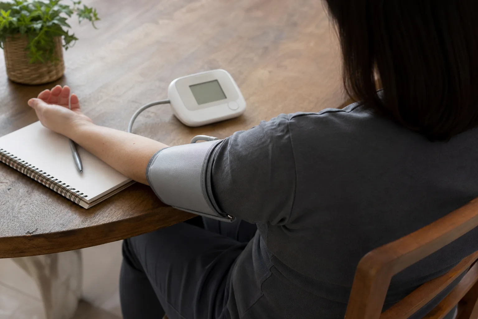 Adult sitting correctly with arm supported while checking blood pressure at home.