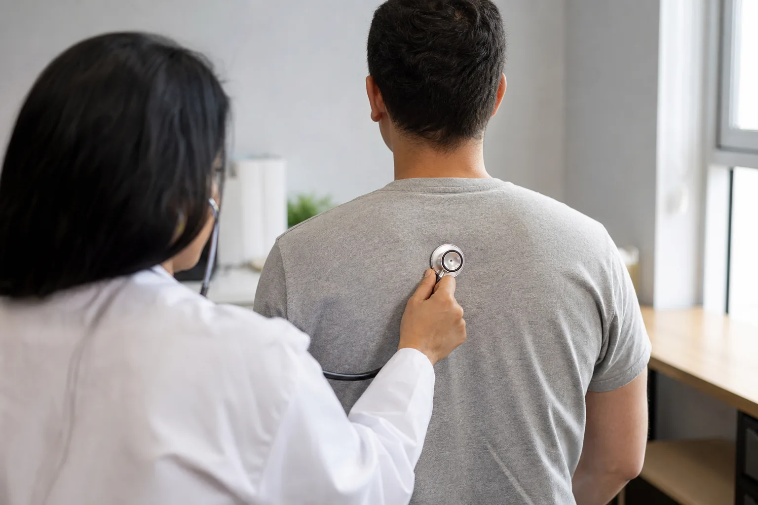 Healthcare professional listening to an adult patient’s lungs during an exam.